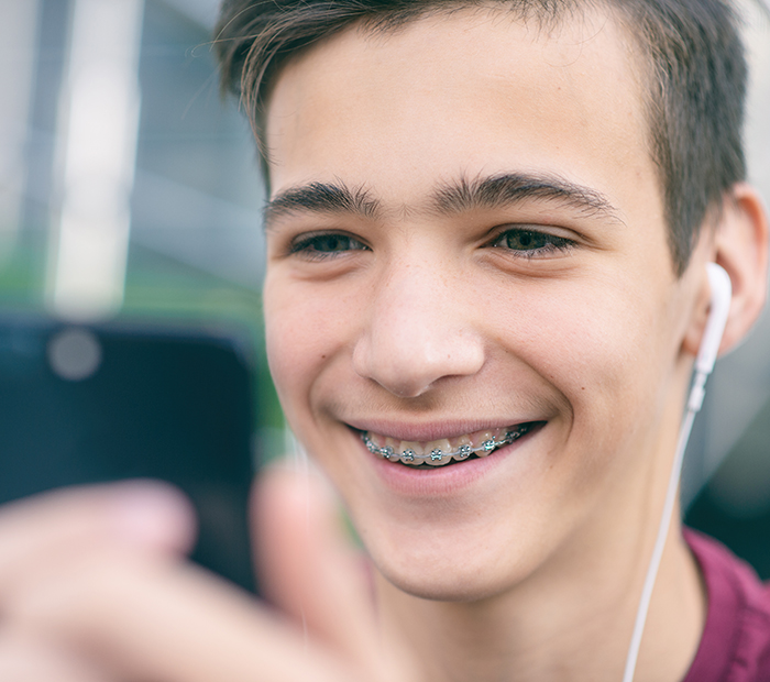 Adolescent avec des broches métalliques regarde son téléphone | Orthodontie des Laurentides à St Jérôme
